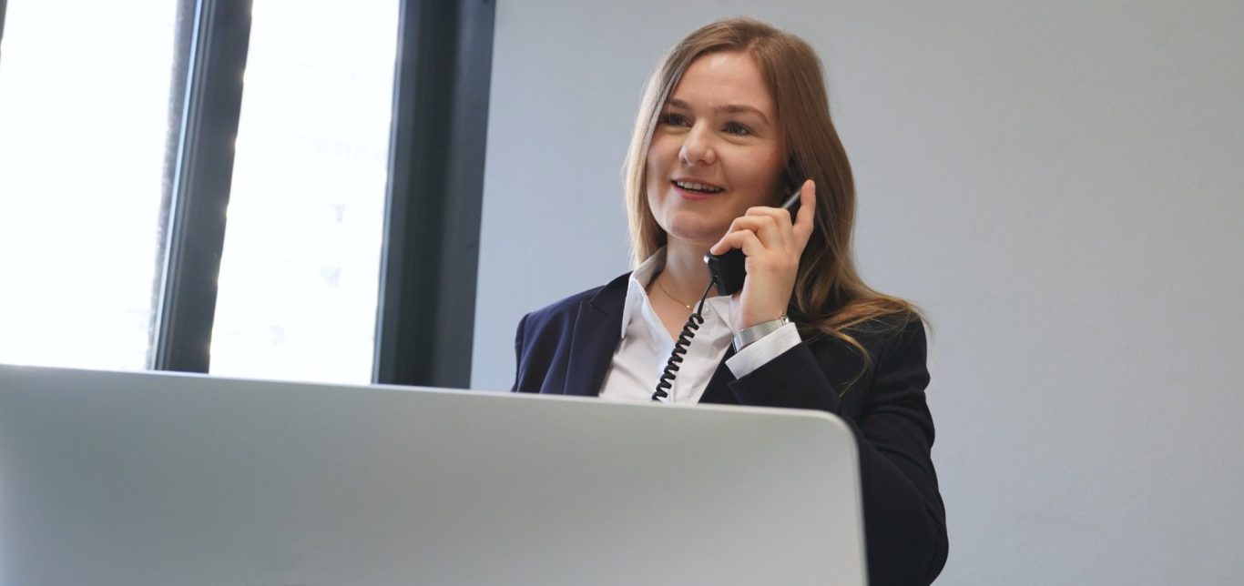 Frau mit Telefon im Büro, lächelnd und in einem Anzug gekleidet.